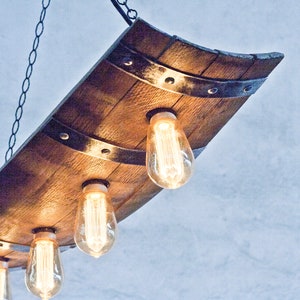 May include: A rustic wooden chandelier with four Edison bulbs hanging from a chain. The chandelier is made from a reclaimed wine barrel stave and has metal accents.