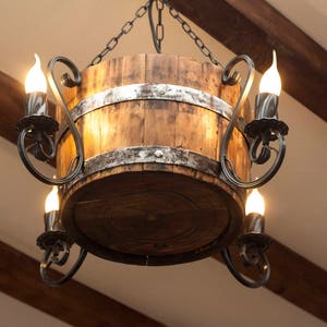 May include: A rustic wooden barrel chandelier with a black metal frame and multiple light bulbs. The chandelier is hanging from a chain.