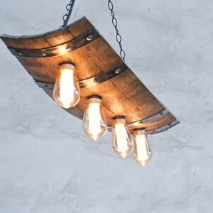 May include: A rustic wooden chandelier with four Edison bulbs hanging from a chain. The chandelier is made from a repurposed wine barrel stave.