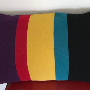 May include: A long rectangular pillow with a striped pattern in teal, purple, red, yellow, teal, black, and blue.