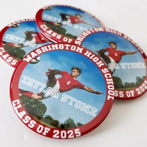 May include: Four red and white round buttons with a soccer player in action. The buttons have the text "WASHINGTON HIGH SCHOOL", "CLASS OF 2025", and "TAYLOR STONE". The background is a blue sky with trees.