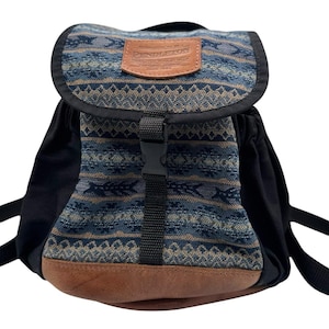 May include: A backpack featuring a blue and tan patterned fabric flap with a brown leather Pendleton patch. The bag has black side panels, a black plastic buckle closure, and a brown leather base. The flap displays the text Pendleton Portland Oregon.