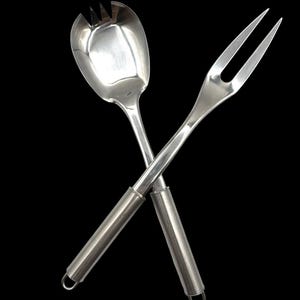 May include: A pair of stainless steel salad serving utensils consisting of a wide, slotted spoon and a long, two-pronged fork. Both utensils feature smooth, polished metal heads and cylindrical handles with small loops at the ends for hanging.