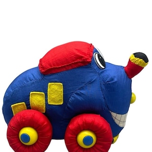 May include: A blue and red plush toy car with yellow wheels and a smiling face. The car has a red roof and yellow details on the side.
