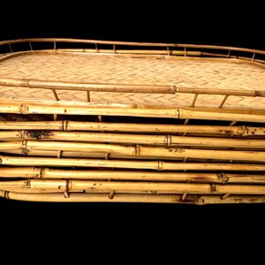 May include: A handcrafted bamboo serving tray with a woven base and a raised rim. The tray is made of natural bamboo, showcasing its warm, light brown color and unique texture. The tray is ideal for serving food or drinks.