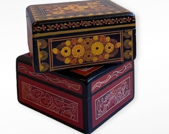 May include: Two decorative wooden boxes with intricate painted designs. The top box features a black background with gold and yellow floral patterns. The bottom box has a red background with black and gold geometric patterns.