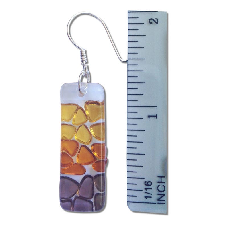 May include: A pair of glass earrings with a silver hook. The earrings are rectangular and feature a mosaic design of yellow, orange, and brown glass pieces. The earrings are approximately 1 inch long.