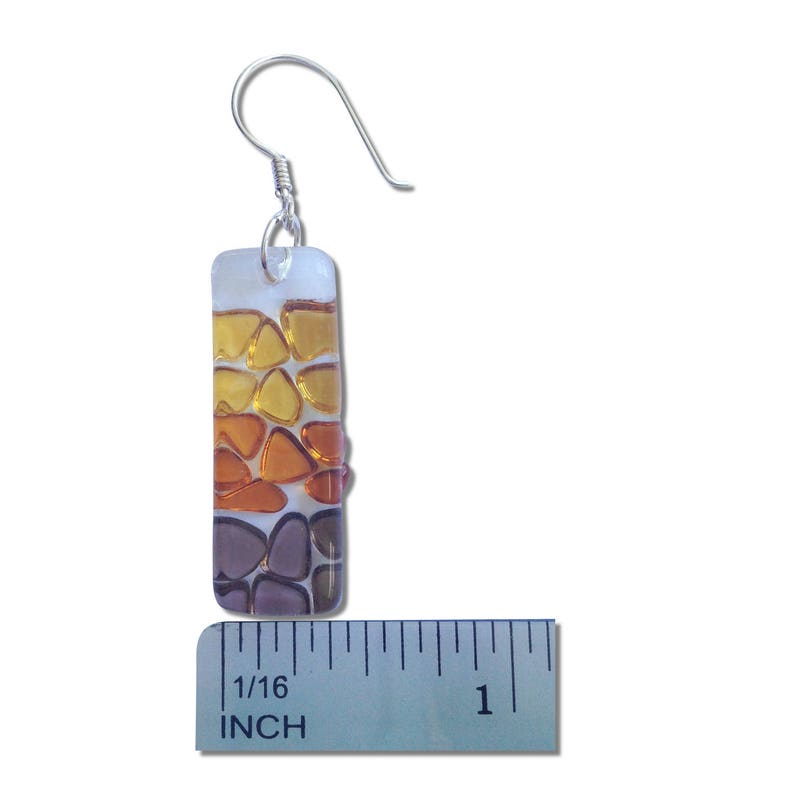 May include: A pair of glass earrings with a silver hook. The earrings are rectangular and feature a mosaic of small, colorful glass pieces in shades of purple, orange, and yellow. The earrings measure 1/16 inch in length.