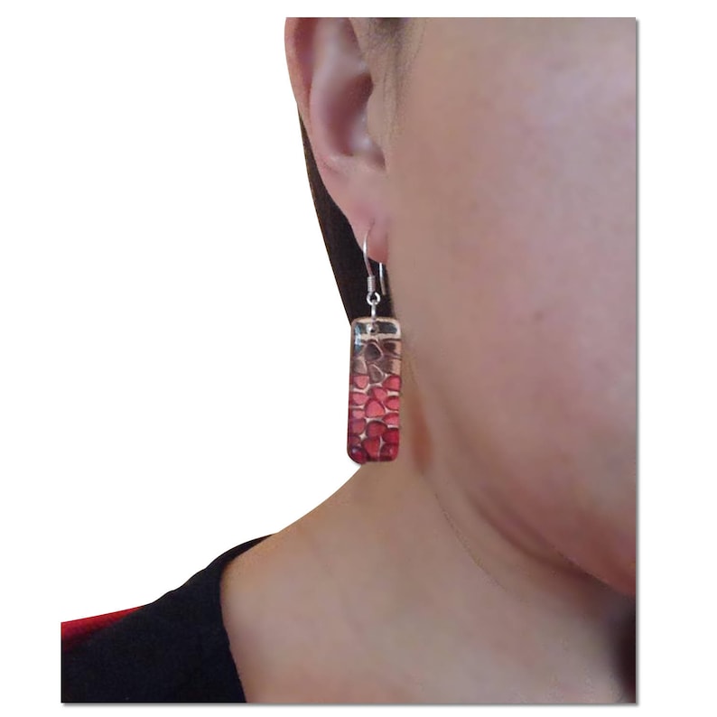May include: A pair of silver dangle earrings with a rectangular red and brown glass pendant. The pendant has a mosaic-like design.