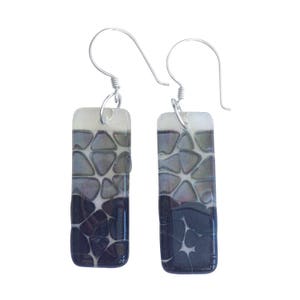 May include: A pair of silver dangle earrings with rectangular glass drops. The glass is clear with a black and gray geometric pattern.