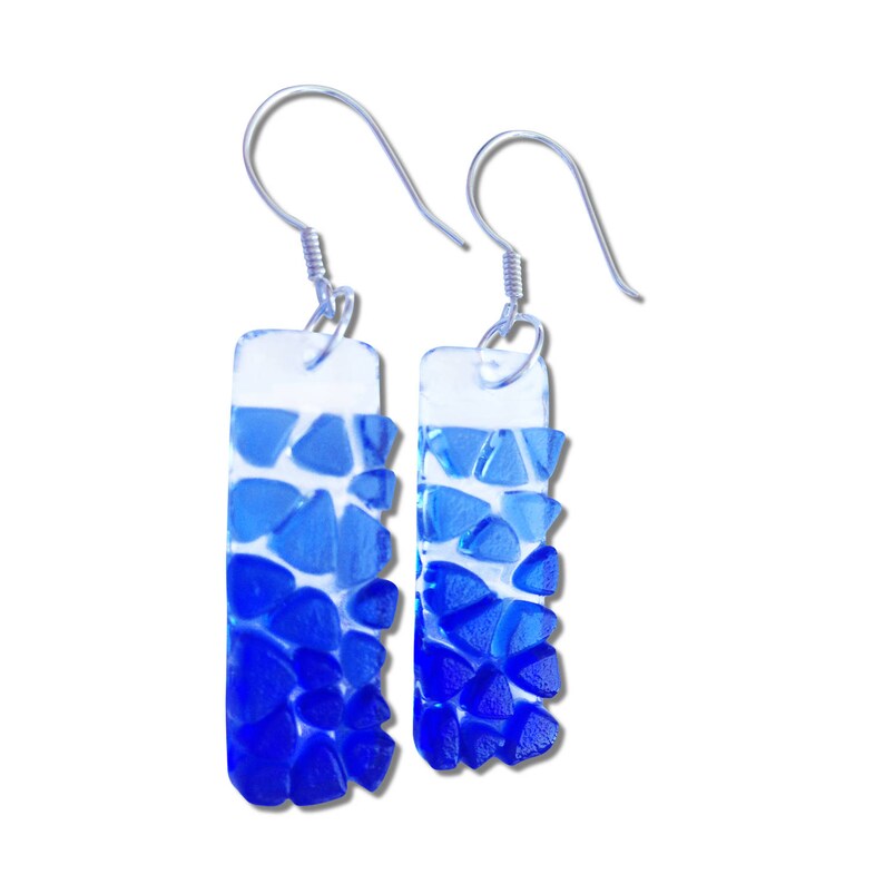 May include: A pair of blue and clear glass earrings with silver hooks. The glass is made up of small, irregular pieces that create a gradient effect from light blue to dark blue.