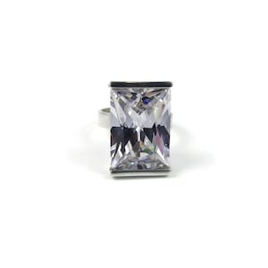 May include: A silver ring featuring a large, clear, rectangular-shaped cubic zirconia stone.