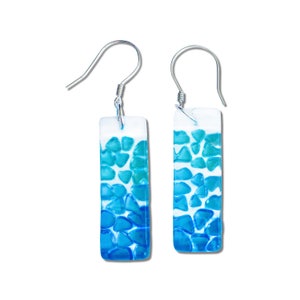 May include: A pair of silver dangle earrings with rectangular blue and white glass pieces. The glass pieces are filled with small, blue, opaque, glass pieces that resemble pebbles.
