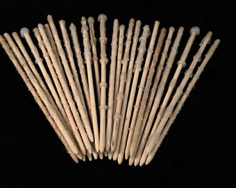 May include: A collection of light-colored wooden wands arranged in a fan shape. Each wand features a unique handle design created with textured, raised material, with some wands displaying rounded tips and others showing tapered, pointed ends.