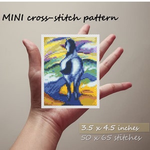 May include: A mini cross-stitch pattern depicting a magpie in blue, white, and black, set against a colorful background. The pattern is 8.9 x 11.4 cm and is labeled "MINI cross-stitch pattern."