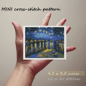 Op de afbeelding: Een kruissteekpatroon van een nachtscène met een straat die is omzoomd met gebouwen en een sterrenhemel. Het patroon is 4,5 x 3,5 inch en heeft 62 x 50 steken.
