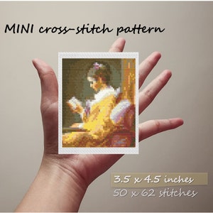 Puede incluir: Un patrón de punto de cruz de una mujer con un vestido amarillo sentada en una silla y leyendo un libro. El patrón mide 3,5 x 4,5 pulgadas y tiene 50 x 62 puntos.