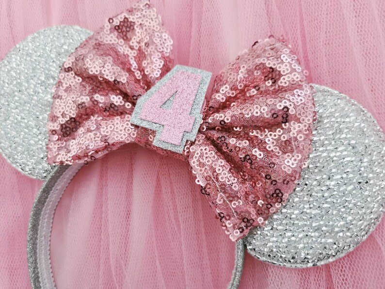 Pu&ograve; includere: Fascia per capelli con glitter rosa e argento con un fiocco rosa e il numero "4" su di essa. La fascia &egrave; progettata per assomigliare alle orecchie di Topolino.