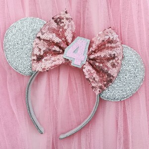 Pu&ograve; includere: Fascia per capelli con orecchie di topo in glitter argento, con un fiocco di paillettes rosa e un numero 4 in feltro rosa.