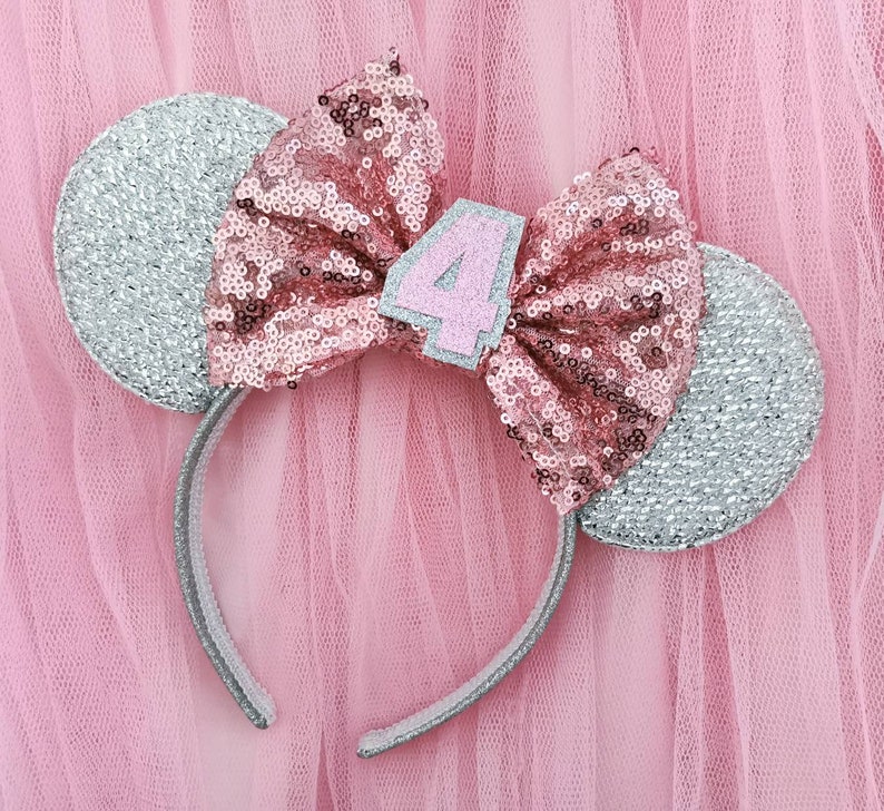 Pu&ograve; includere: Fascia per capelli con orecchie di topo in glitter argento, con un fiocco di paillettes rosa e un numero 4 in feltro rosa.