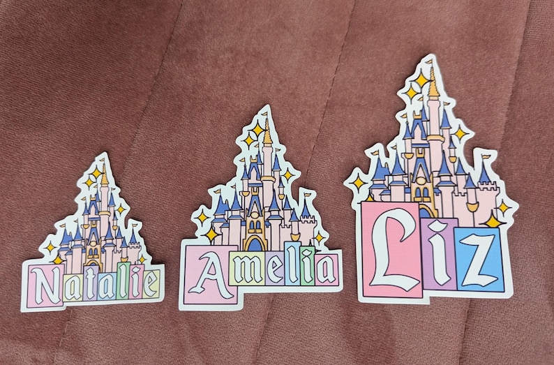 Puede incluir: Tres pegatinas troqueladas con una ilustraci&oacute;n de un castillo rosa y azul con estrellas amarillas. Cada pegatina muestra un nombre en fuente de bloque: Natalie, Amelia y Liz. Los dise&ntilde;os tienen un borde blanco y bloques de color pastel.