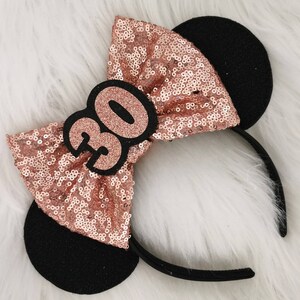 Pu&ograve; includere: Fascia per capelli con paillettes oro rosa, orecchie di topo nere e un numero 30 in feltro nero sul fiocco.