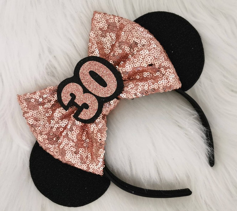 Pu&ograve; includere: Fascia per capelli con paillettes oro rosa, orecchie di topo nere e un numero 30 in feltro nero sul fiocco.