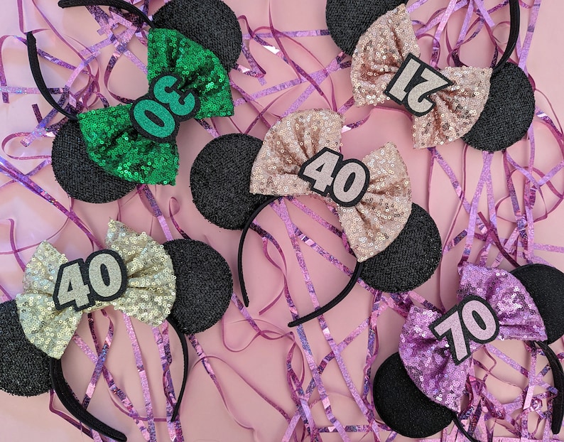 Pu&ograve; includere: Cinque paia di orecchie di topo nere con fiocchi di paillettes. I fiocchi sono di colori diversi e hanno numeri su di essi: 30, 40, 70, 21 e 40.