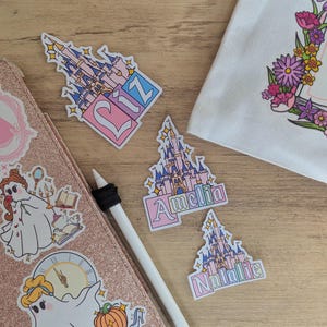 Puede incluir: Una colecci&oacute;n de pegatinas troqueladas con castillos de cuento de hadas en rosa y azul con los nombres Liz, Amelia y Natalie. Otras pegatinas incluyen un fantasma con vestido, un reloj y una bolsa blanca con el texto Believe In your own Fairy Tale.