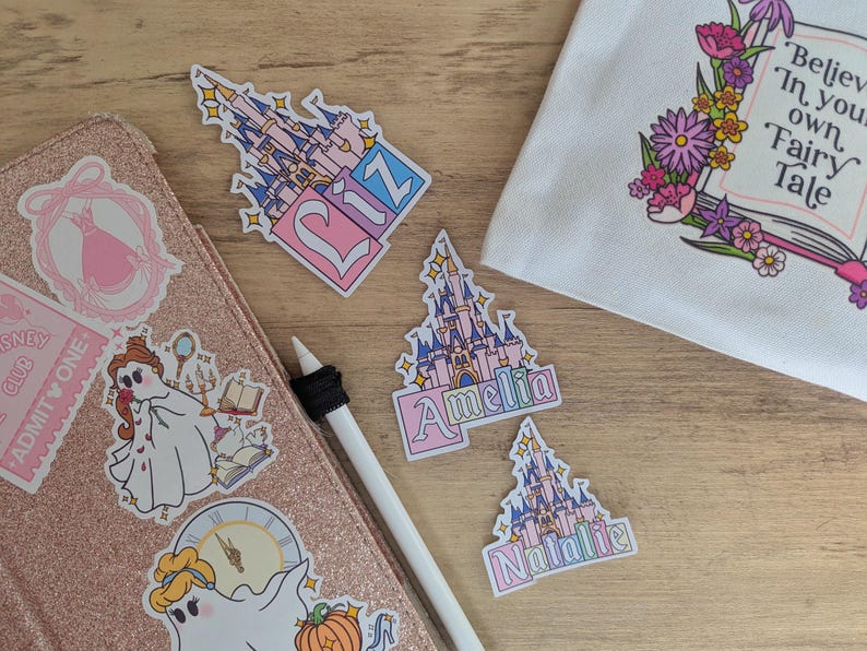 Puede incluir: Una colecci&oacute;n de pegatinas troqueladas con castillos de cuento de hadas en rosa y azul con los nombres Liz, Amelia y Natalie. Otras pegatinas incluyen un fantasma con vestido, un reloj y una bolsa blanca con el texto Believe In your own Fairy Tale.