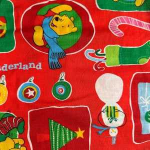 May include: Red fabric with a Christmas theme featuring Winnie the Pooh and Piglet. The fabric has a variety of Christmas images including ornaments, candy canes, a snowman, a Christmas tree, and presents. The text "Wonderland" is printed on the fabric.