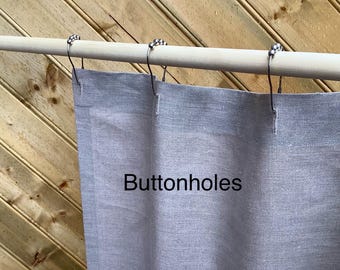 Puede incluir: Una cortina de ducha de lino gris con ojales y ganchos de metal plateado colgados de una barra de madera.