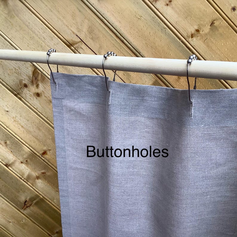 May include: A gray linen shower curtain with buttonholes and silver metal hooks hanging from a wooden rod.
