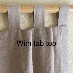 May include: Two beige linen curtains with tab tops hanging on a wooden rod. The text "With tab top" is written on the curtains.