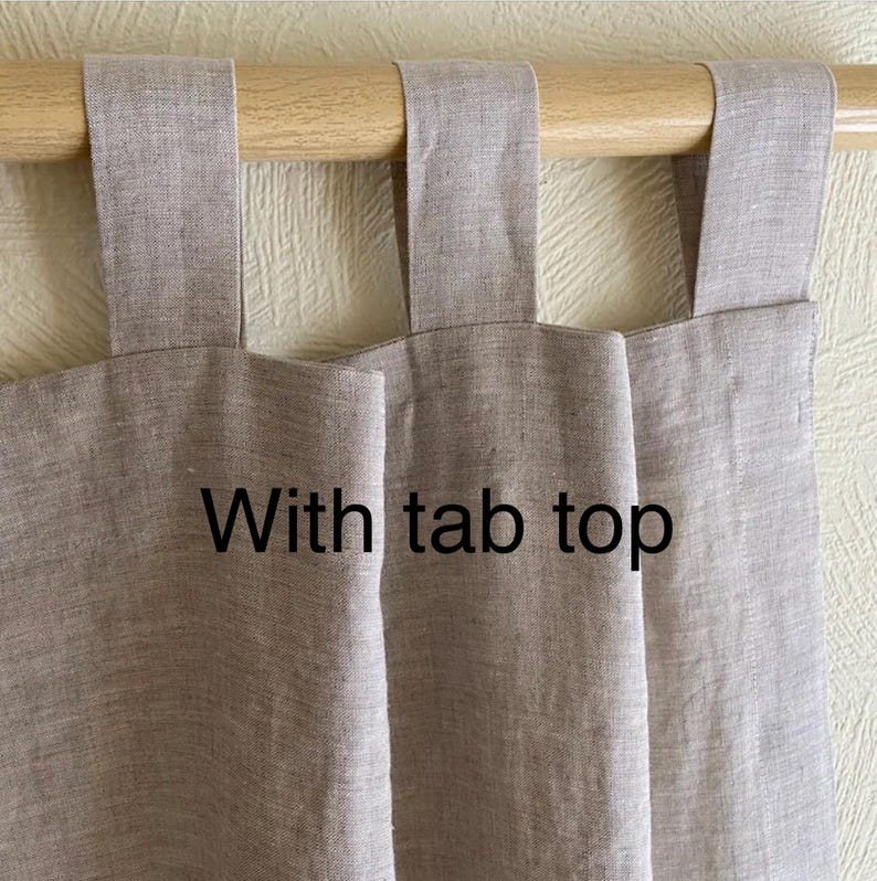 May include: Two beige linen curtains with tab tops hanging on a wooden rod. The text "With tab top" is written on the curtains.