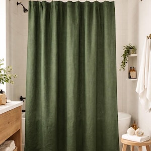 May include: A solid olive green shower curtain hangs in a bathroom. The curtain is made of a textured fabric and is suspended from a gold-colored rod. The bathroom has white tile walls and a wooden vanity.