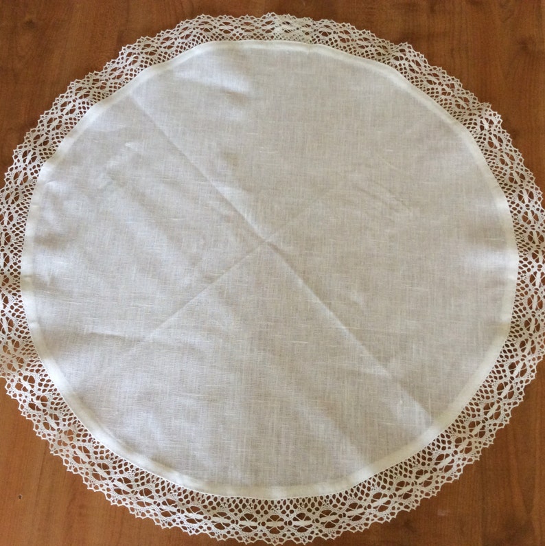 Puede incluir: Mantel redondo blanco con un delicado borde de encaje. El mantel est&aacute; hecho de una tela suave, similar al lino.