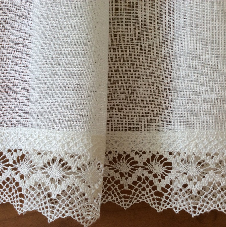 May include: White sheer curtains with a delicate lace trim. The curtains are made of a lightweight fabric and have a subtle texture.