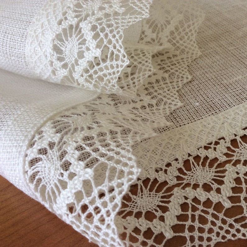 May include: White linen fabric with a delicate white lace trim. The lace is intricate and has a floral pattern.
