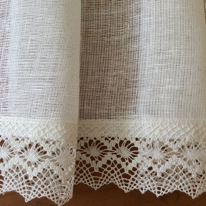 May include: White sheer curtains with a delicate white lace trim. The lace has a floral pattern.