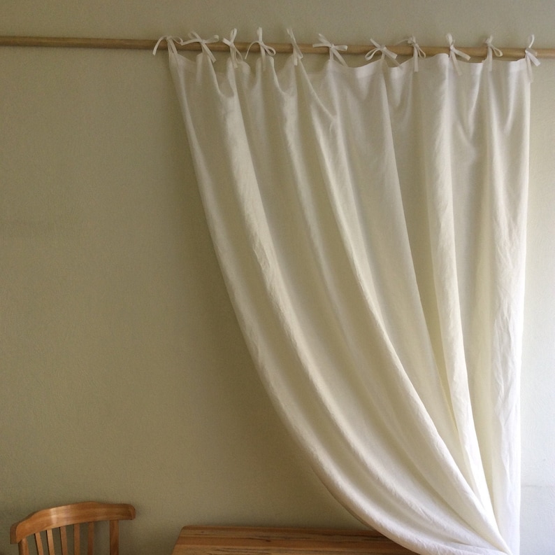May include: White linen curtains with a gathered top and a simple, elegant design. The curtains are hung on a wooden rod and are gathered at the top with ties.