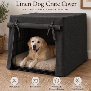 Pode incluir: Uma capa de linho cinza-carvão escuro para gaiola de cão com painel frontal enrolável fixado por dois laços de tecido. A capa cobre uma gaiola de arame preta contendo um cão de cor dourada clara deitado numa cama bege felpuda.