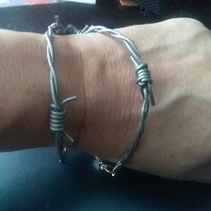 May include: A silver barbed wire bracelet worn on a person's wrist.