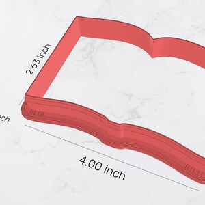 May include: Red plastic cookie cutter shaped like an open book. The cutter is 4 inches wide and 2.63 inches tall. Area is 9.67 square inches.