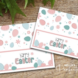 May include: Two printable Easter gift tags with a white background and pink and blue egg designs. The text "Happy Easter" is written in pink and blue on each tag.