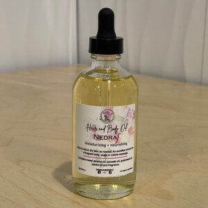 May include: A clear glass bottle with a black dropper top filled with a light yellow liquid. The bottle has a label that reads "Hair and Body Oil NEDRA moisturizing + nourishing Use on wet or dry skin as needed. An excellent choice for a fragrant body, scalp or cuticle massage. Contains sweet almond oil, avocado oil, grapeseed oil, jojoba oil and fragrance."