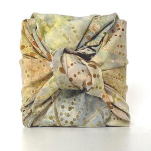 May include: A square package wrapped in a light blue and brown fabric with a white and brown polka dot pattern. The fabric is tied in a knot at the top of the package.