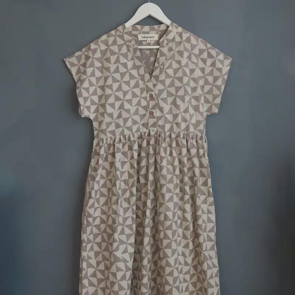 Peut inclure: Robe beige et blanche à imprimé géométrique, manches courtes et col en V. La robe a une taille froncée et est suspendue à un cintre blanc. La robe est faite d'un tissu doux et léger.