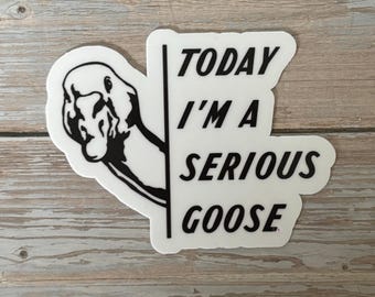 May include: A white sticker with a black and white illustration of a goose and the text "TODAY I'M A SERIOUS GOOSE". The sticker is on a wooden surface.
