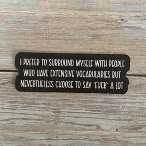 May include: Black rectangular sticker with white text. The text reads: "I PREFER TO SURROUND MYSELF WITH PEOPLE WHO HAVE EXTENSIVE VOCABULARIES BUT NEVERTHELESS CHOOSE TO SAY 'FUCK' A LOT."